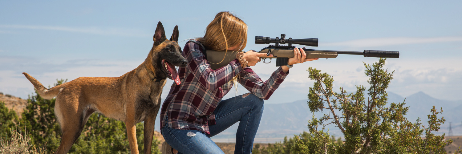 Dog standing behind woman as she aims a rifle with a SilencerCo suppressor