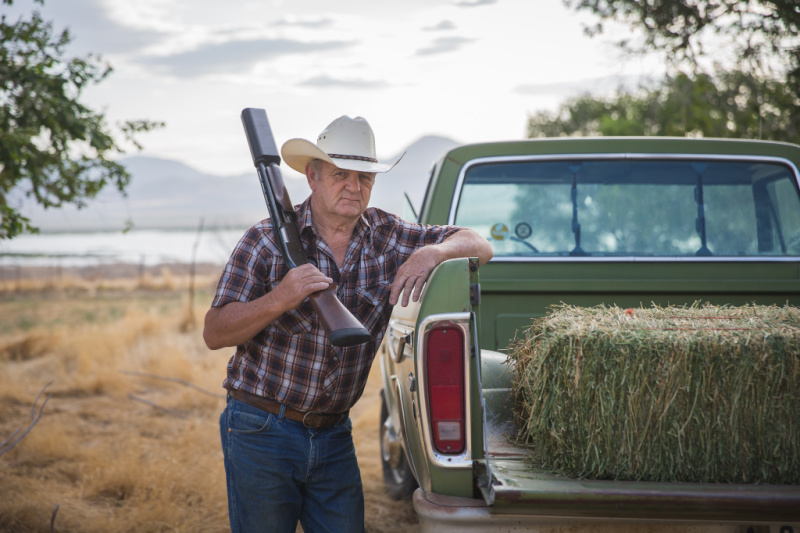 Rancher leaning on farm truck with SilencerCo Salvo suppressed shotgun on his shoulder.