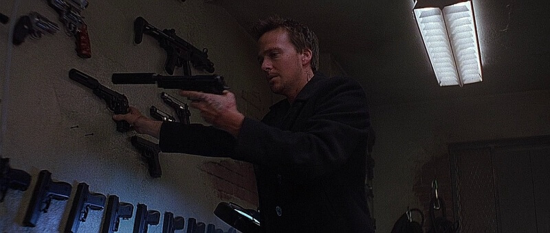 Connor McManus selects a pair of suppressed Beretta 92 pistol from arms dealer wall.
