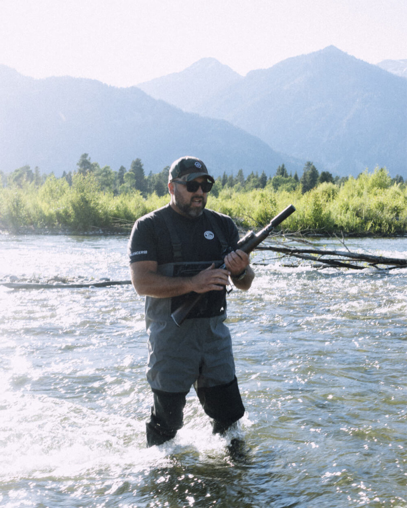 Man standing in river with mountains in background, holding a suppressed lever gun - SilencerCo Spectre 9