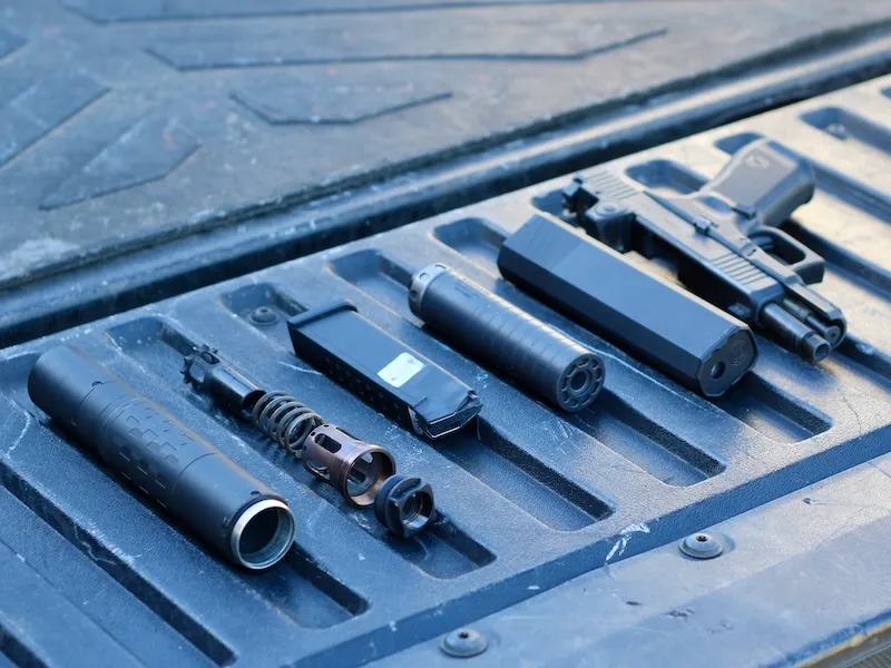 Glock suppressed - Silencerco suppressors, Nielsen device, and Glock pistol laid out on a tailgate