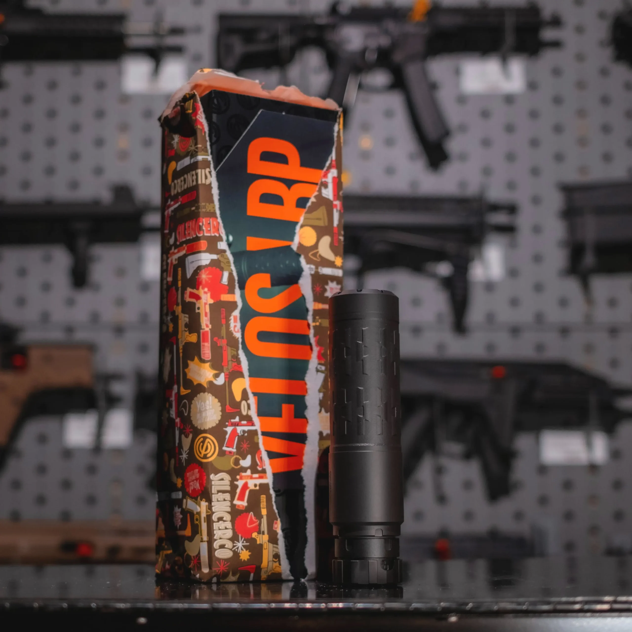 A half opened gift wrapped in SilencerCo Wrapping Paper, displayed next to a gift of a Velos suppressor.
