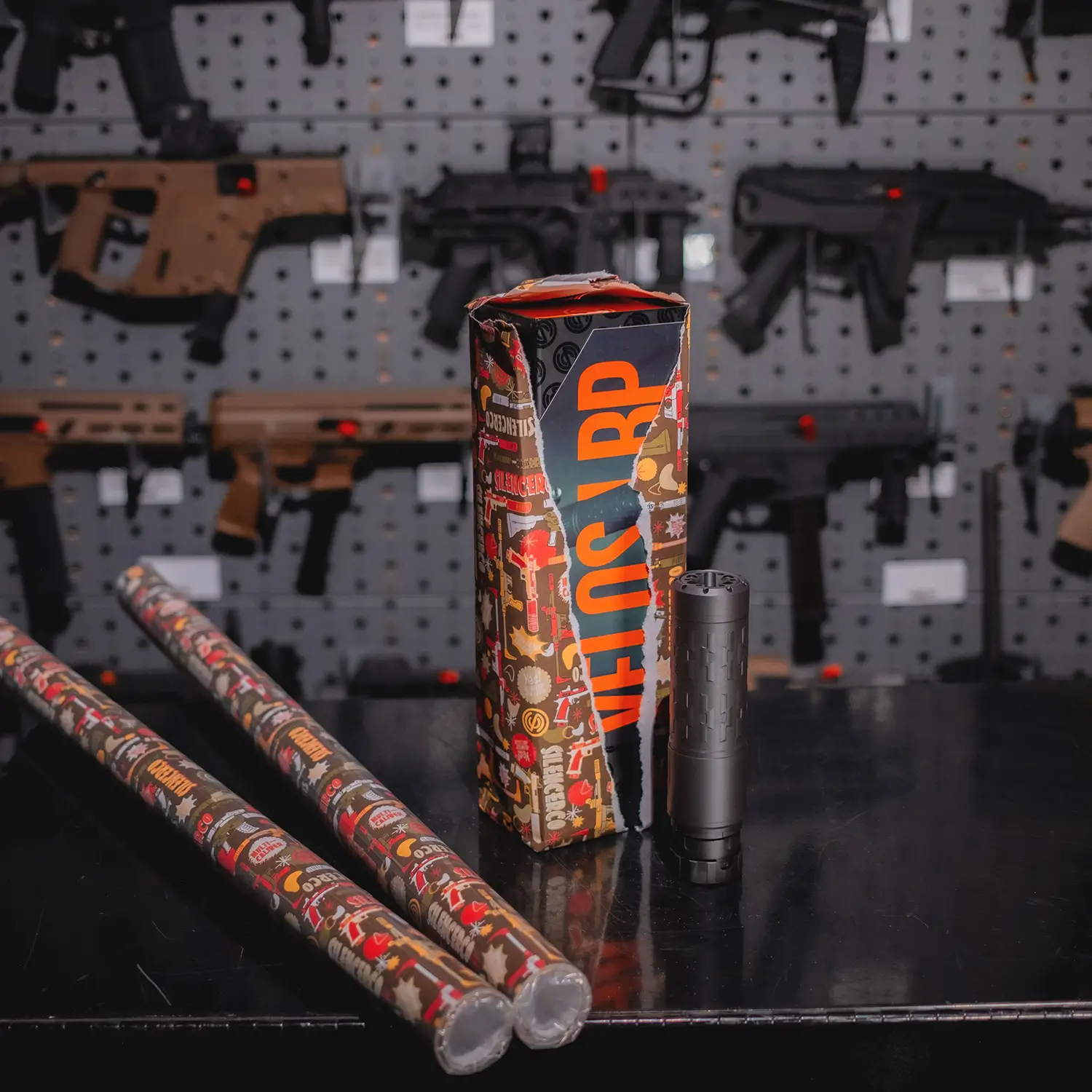 Rolls of Rolls of SilencerCo Wrapping Paper with a halved opened gift of a Velos Suppressor.