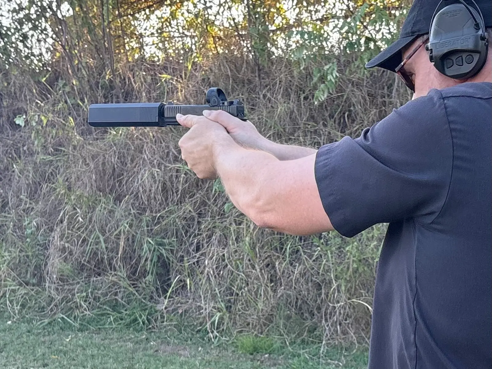 Shooter aiming a suppressed Gen 6 GLOCK with a SilencerCo Osprey 2.0 at an outdoor range.