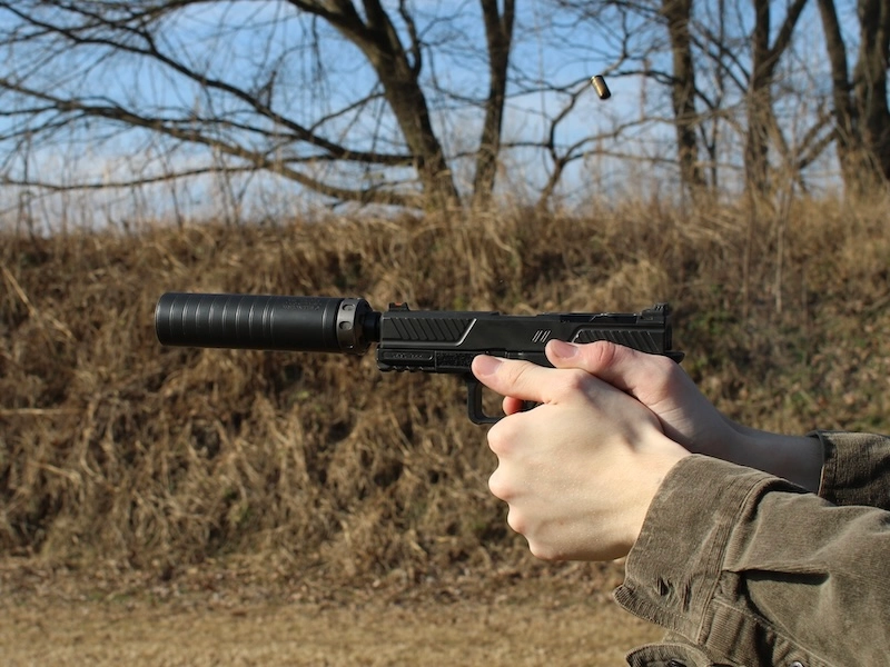 hands shooting suppressed ZEV OZ9 with ejected spent casing flying through the air