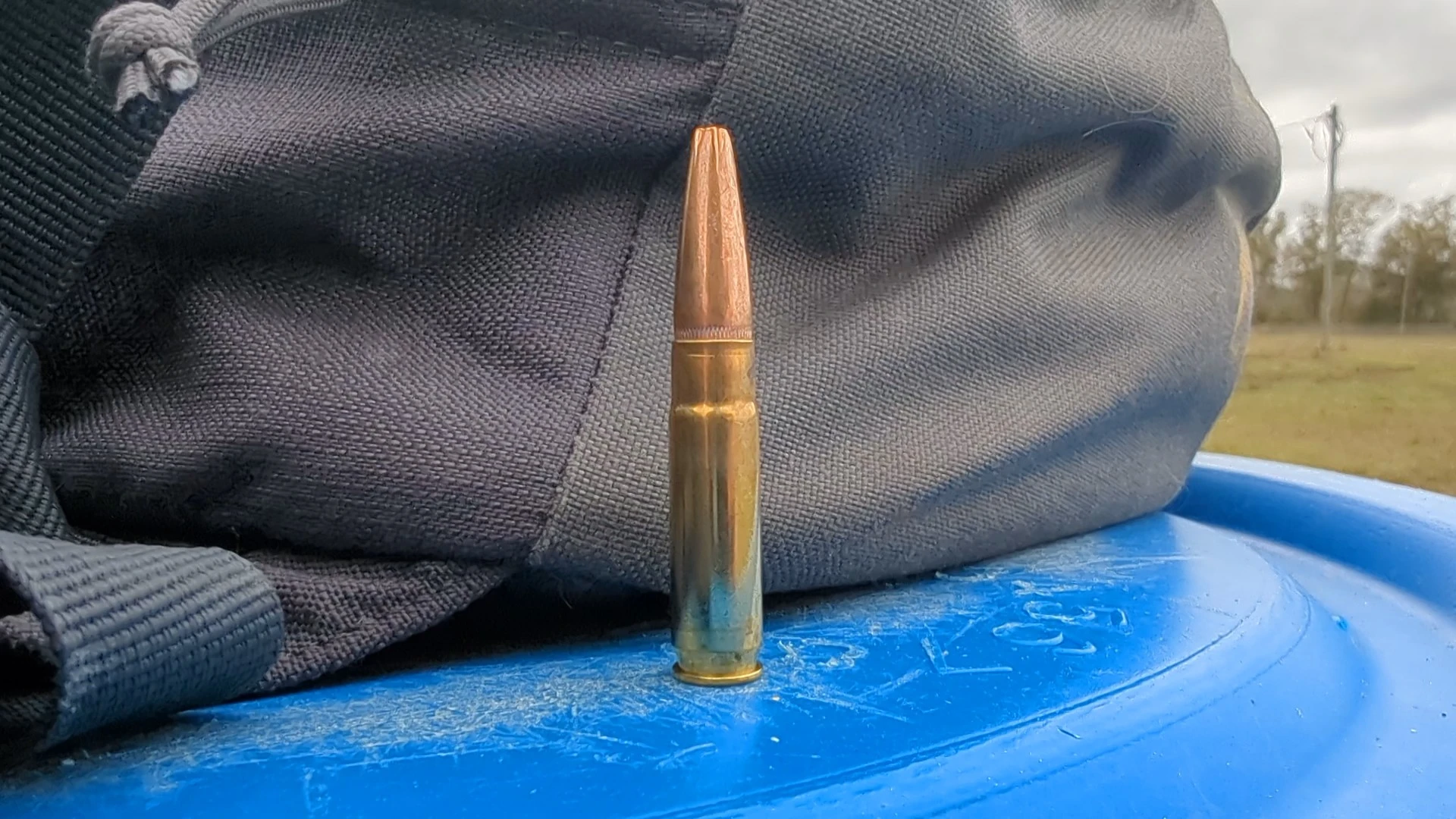 .300 Blackout cartridge on a blue barrel with range bag in the background.