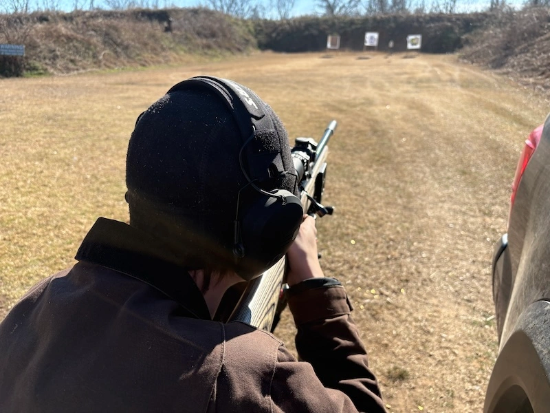 posterior view of shooting aiming a silencerco sparrow suppressed Ruger American Rimfire .22 WMR downrange at paper target