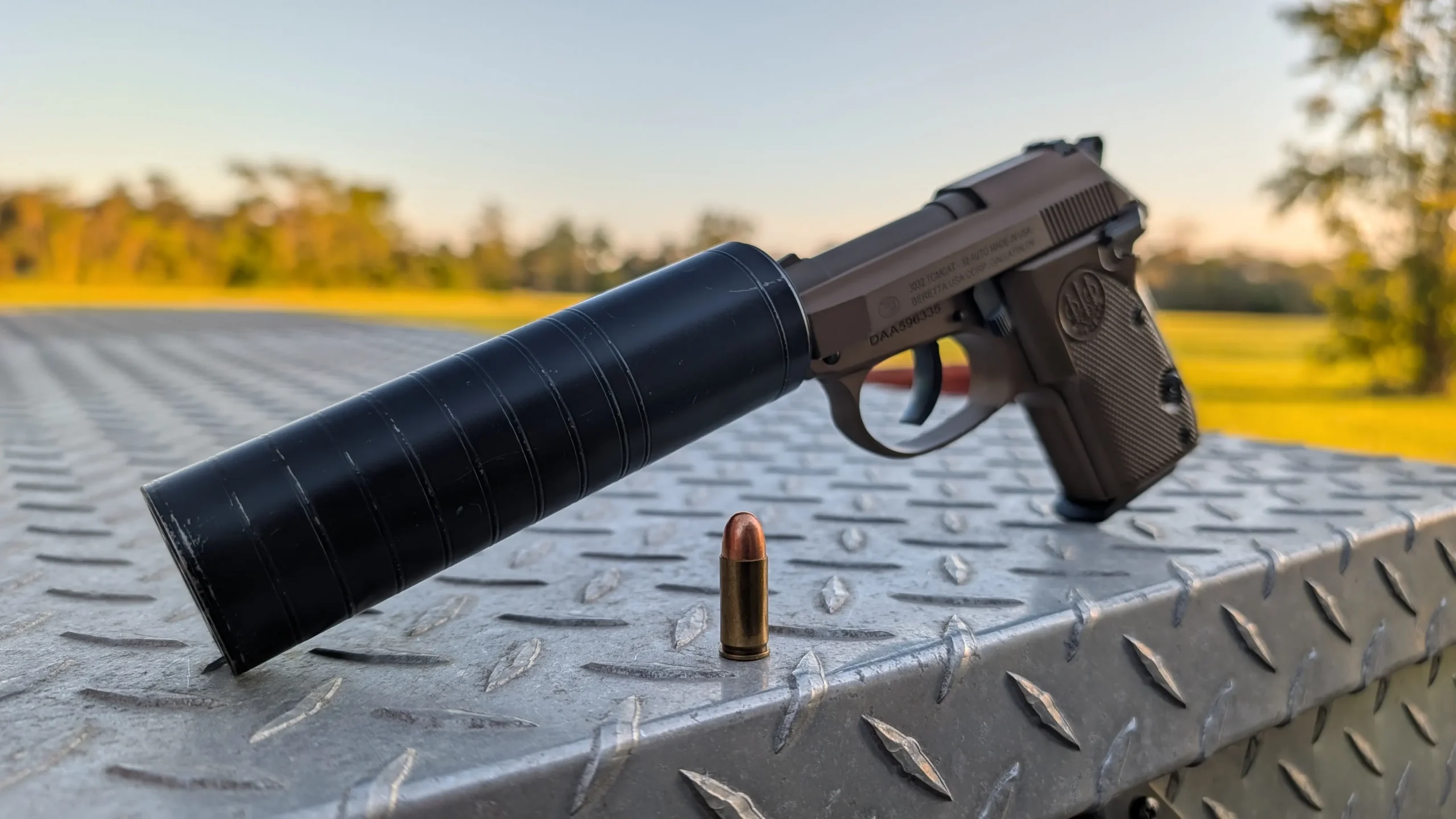 Spectre 9 on 3032 handgun, propped on a truckbed toolbox with a round of 32. ACP standing beside it, to show that a 9mm suppressor works well for the cartridge.