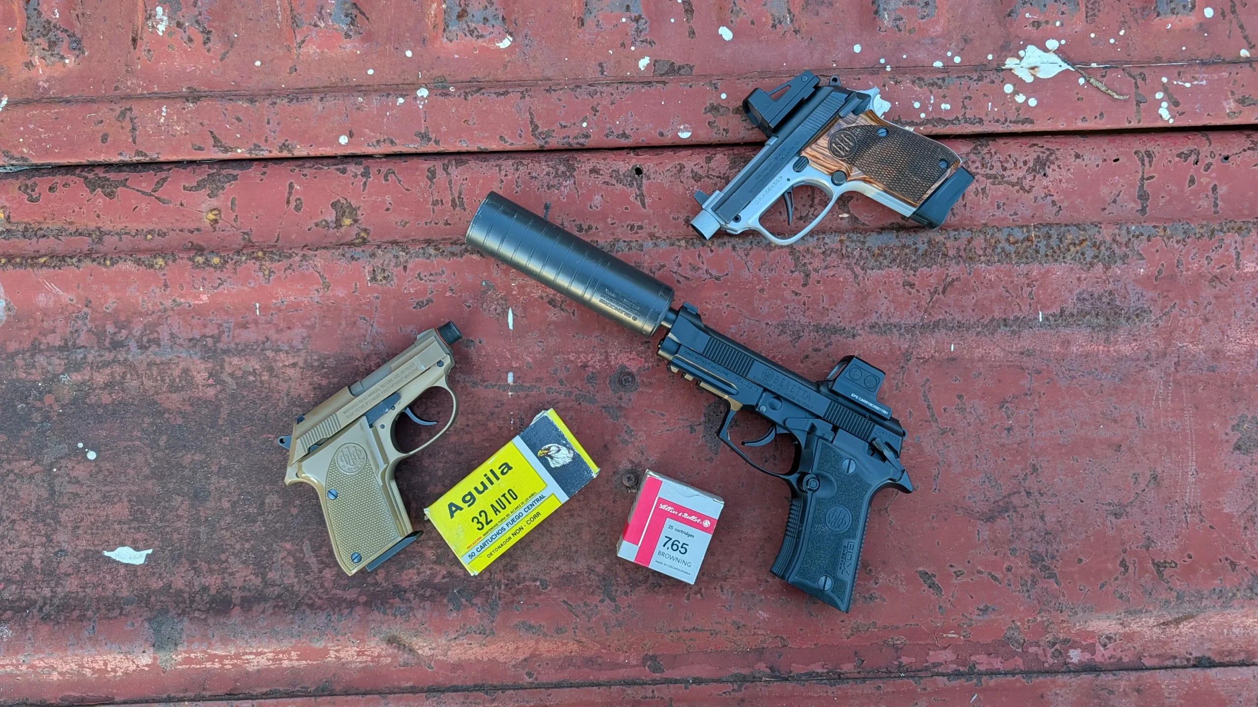 three .32 ACP handguns with suppressor and ammo on a truck bed