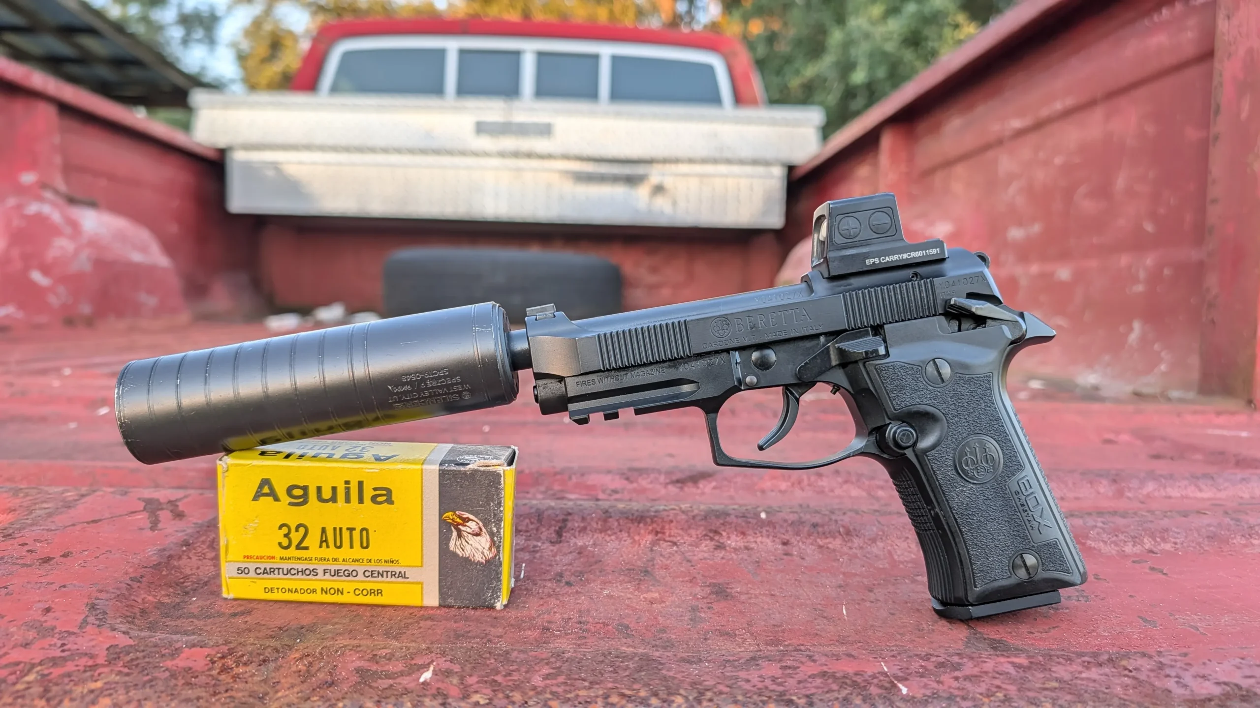 80X suppressed, on a red truck bed, box of Aguila .32 ACP in the foreground.