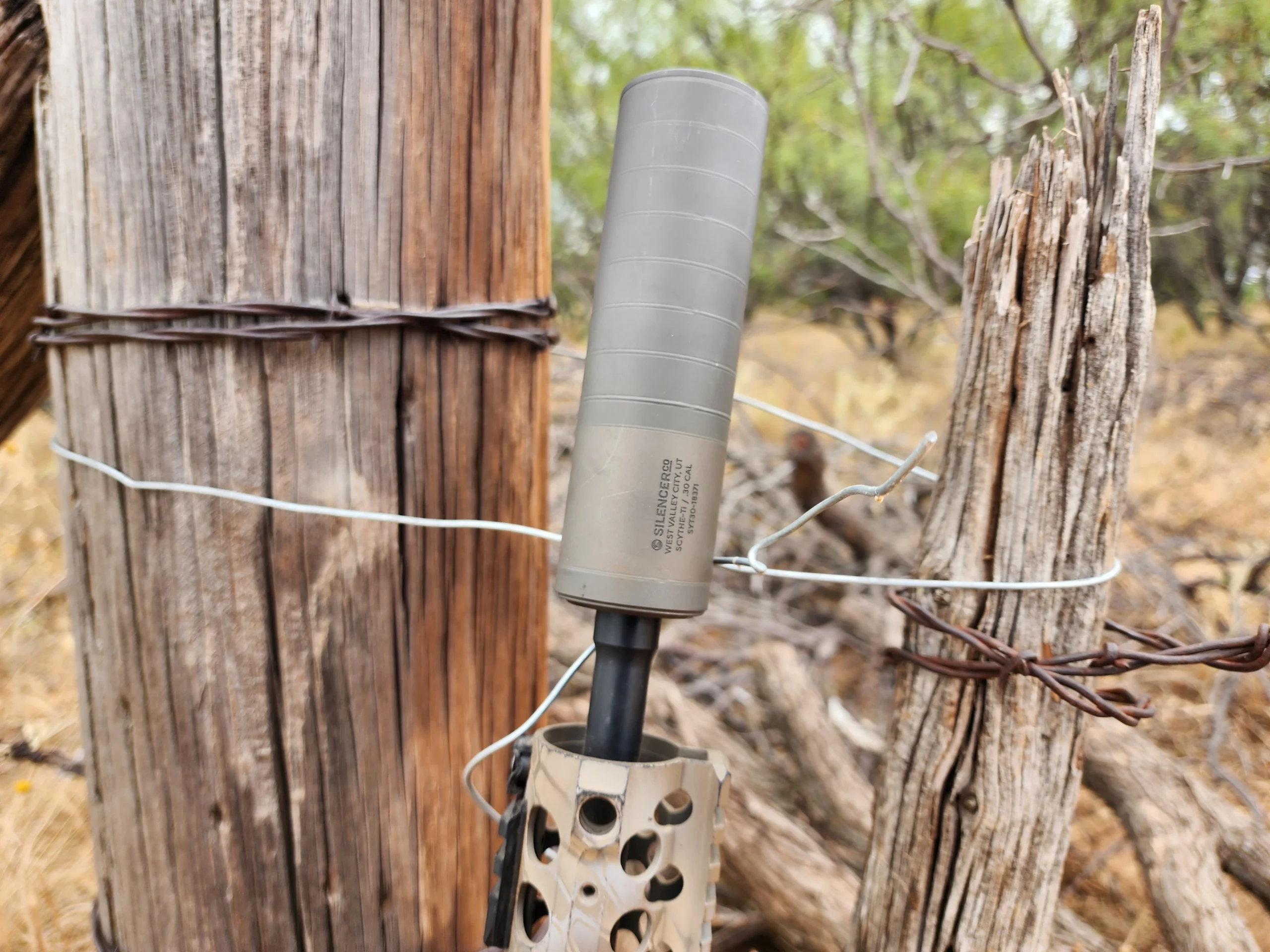scythe-ti suppressor mounted to a deer rifle, leaning against a fence post
